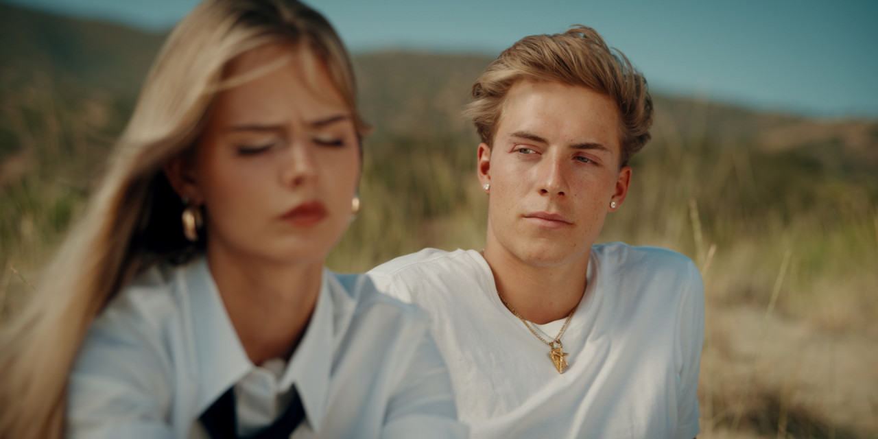 Jonah (Paul Boehme) und Chiara (Sara Crumbleleg) sitzen am Strand. Frame aus Prime Video Serie 'Die neue Generation Krass Klassenfahrt'.