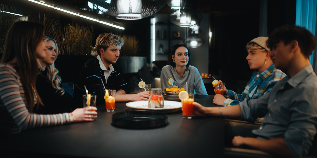 Gruppe sitzt am Tisch und trinkt. Frame aus Prime Video Serie "TOXISCH".