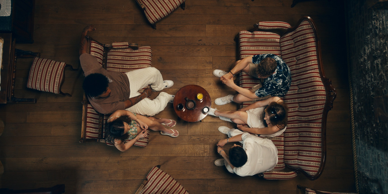 Topdown: Gruppe sitzt im Wohnzimmer. Frame aus RTL+ Serie "Villa der Liebe".