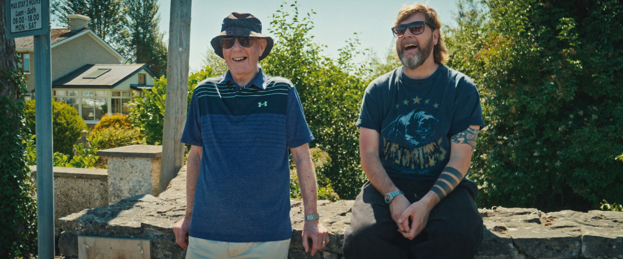 Rea Garvey und Vater sitzen auf Mauer. Frame aus Doku "You'll be Grand".